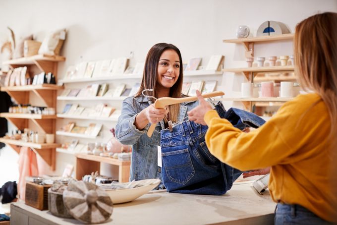eCommerce fashion store merchant handing a pair of blue jeans to a collection customer
