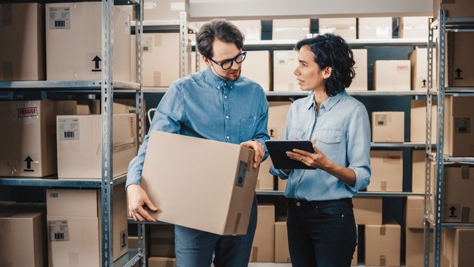 Female Inventory Manager Shows Digital Tablet Information to a Worker Holding Cardboard Box