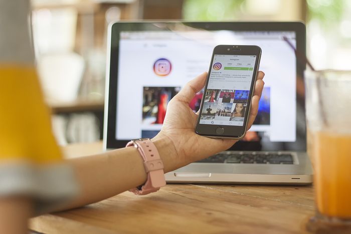 Shopify store owner holding a cell phone in front of a laptop depicting an Instagram feed