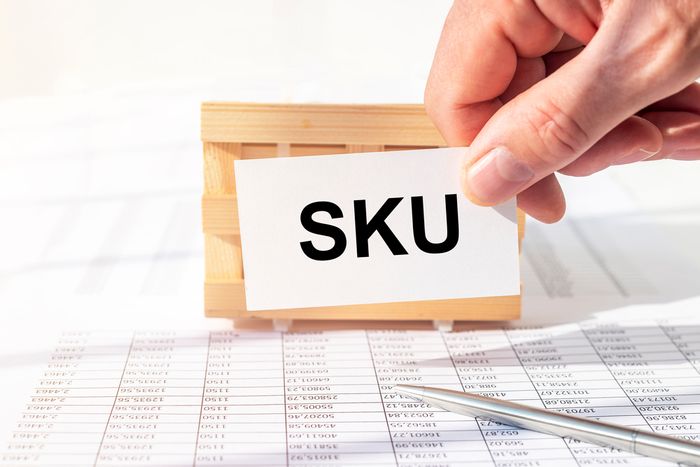 Hand holding a card with the word "SKU" on it in front of a small box and SKU numbers