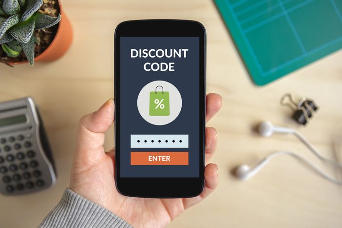 A close-up of a smartphone in a person's hand with the screen that reads "Discount Code" with a graphic of a shopping bag marked with % below