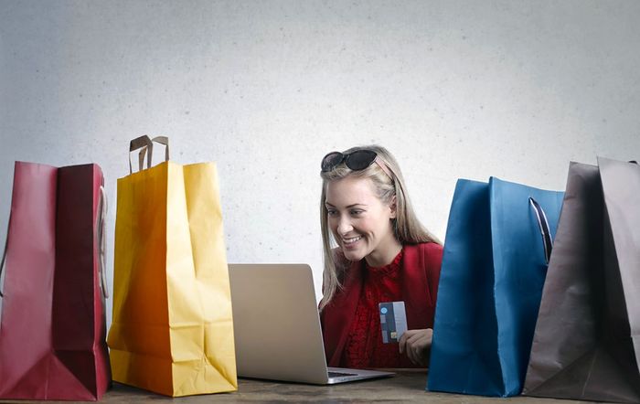 a woman sitting in front of a laptop computer surrounded by shopping bags