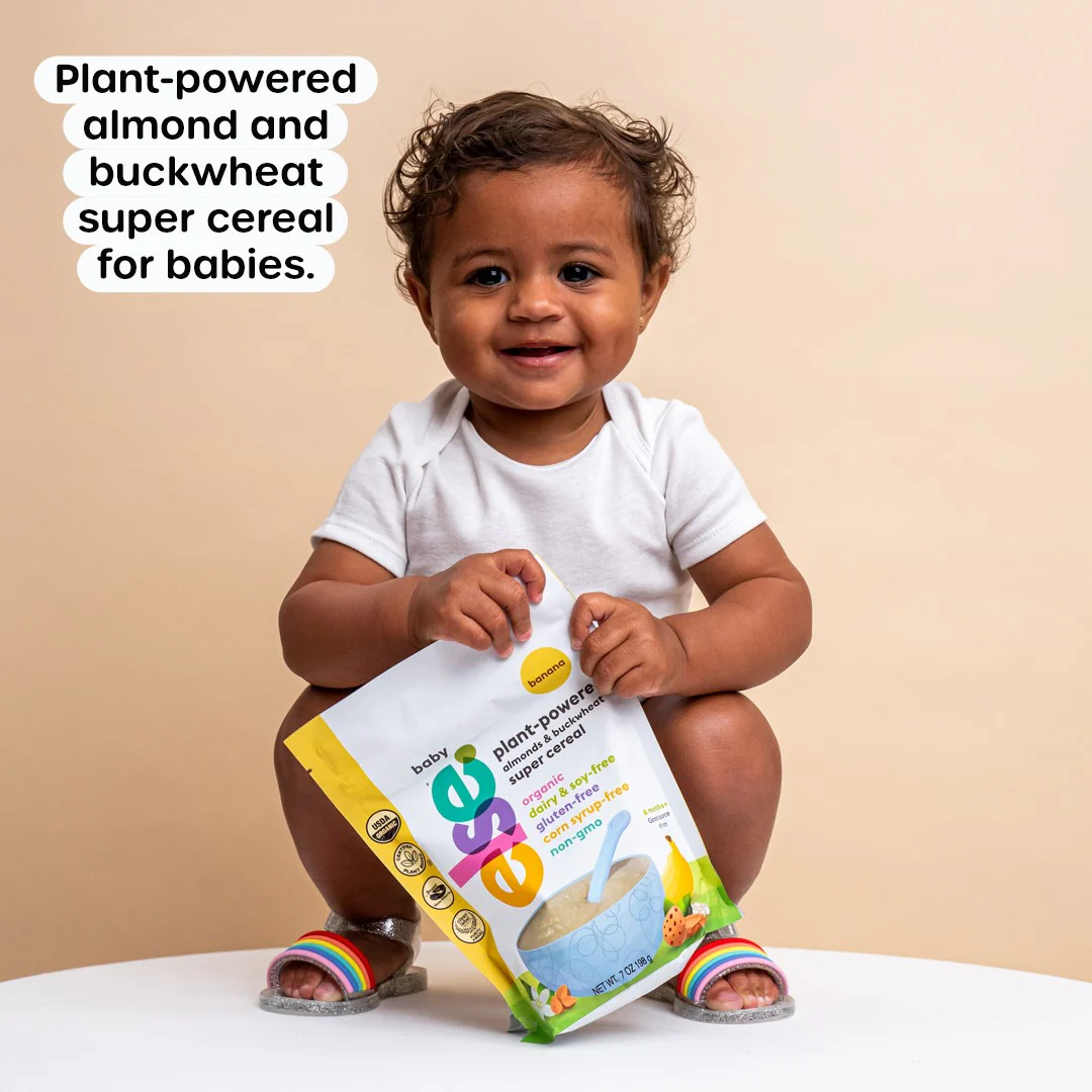 a baby sitting on a table holding a bag of cereal