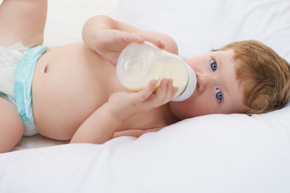 A baby in a diaper drinking from a bottle.