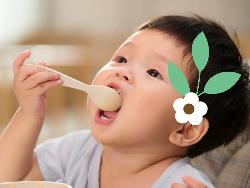 a young child eating from a spoon with a flower on him.