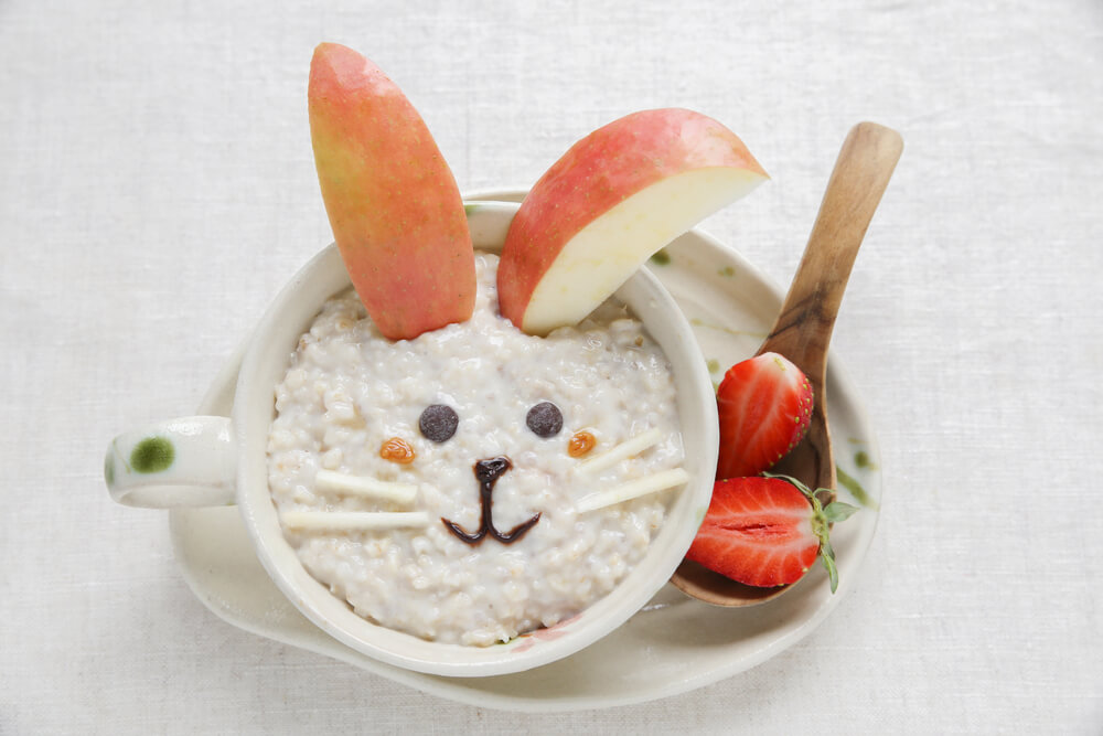 A bowl of porridge with a bunny face made out of fruit.