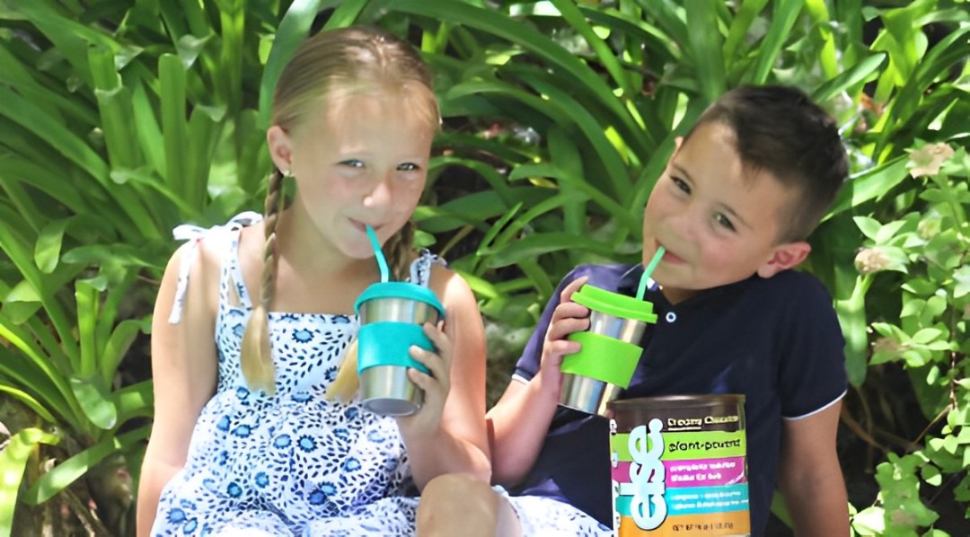 A boy and a girl sitting next to each other drinking smoothies with a tub of Else Nutrition Shake.