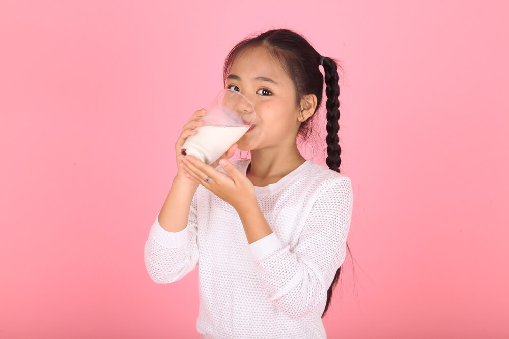 A little girl drinking a glass of soy milk.