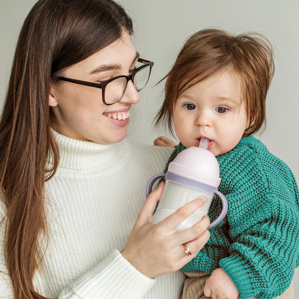 a woman holding a baby while holding a sippy cup