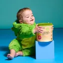 a baby in a green dinosaur costume playing with a can of baby food