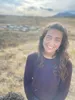 a woman standing in a field with mountains in the background