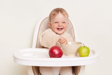 A baby sitting in a high chair eating a bowl of food.