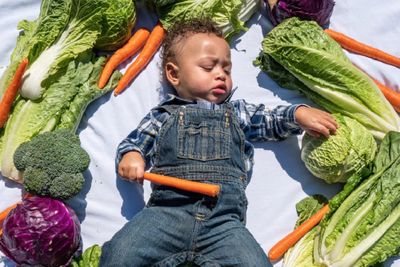 a little boy laying on a blanket with lots of vegetables