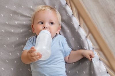 A baby laying on a bed drinking from a bottle.