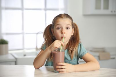 A little girl drinking a weight-gaining protein shake for kids.