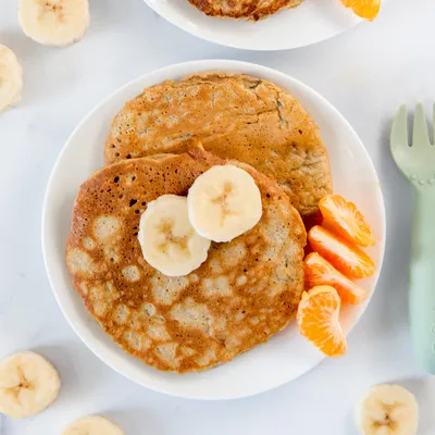a plate of pancakes with bananas and orange slices