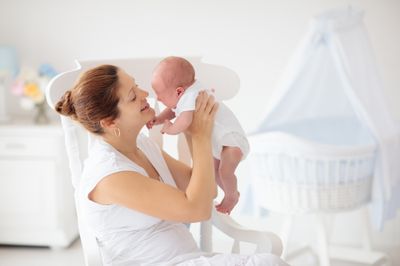 A woman holding a baby in a white nursery.