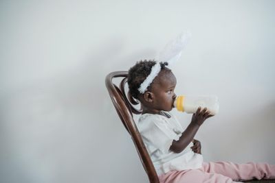 a little girl sitting in a chair drinking from a bottle