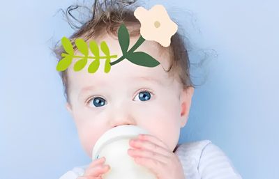 A baby drinking from a cup with a white flower on their head.