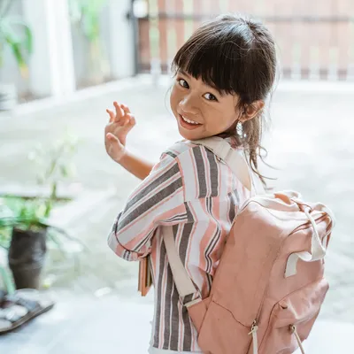 girl with a pink backpack waving at the camera