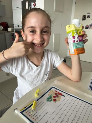 a young girl giving a thumbs up while sitting at a table