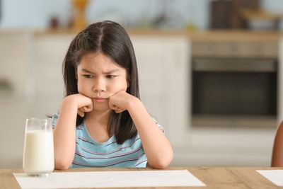 a little girl sitting at a table with a glass of milk