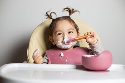 A little girl sitting in a high chair with a spoon in her mouth.