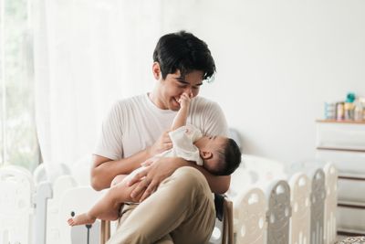 a man holding and feeding a baby while sitting in a chair