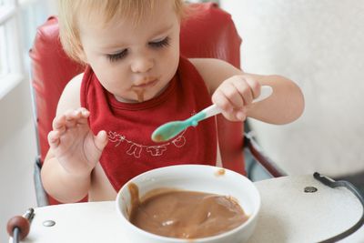 a baby in a high chair eating baby cereal from a bowl