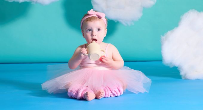 a baby girl in a pink tutu sitting on a blue background