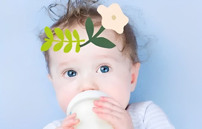 A baby drinking from a cup with a white flower on their head.