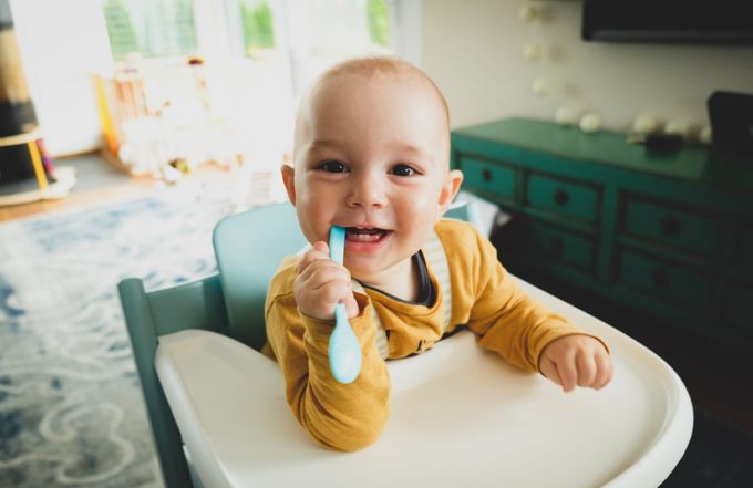 a baby sitting in a high chair holding a toothbrush