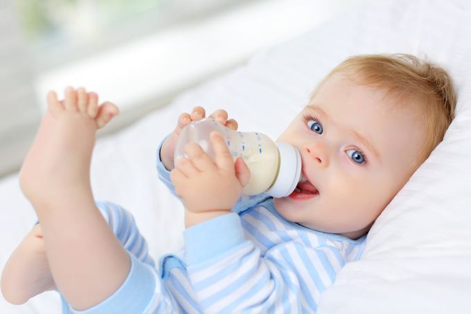 a baby laying on a bed drinking from a bottle.