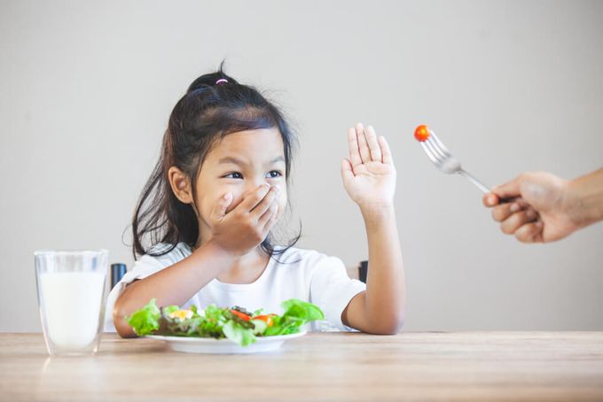 a little girl sitting at a table with a plate of food