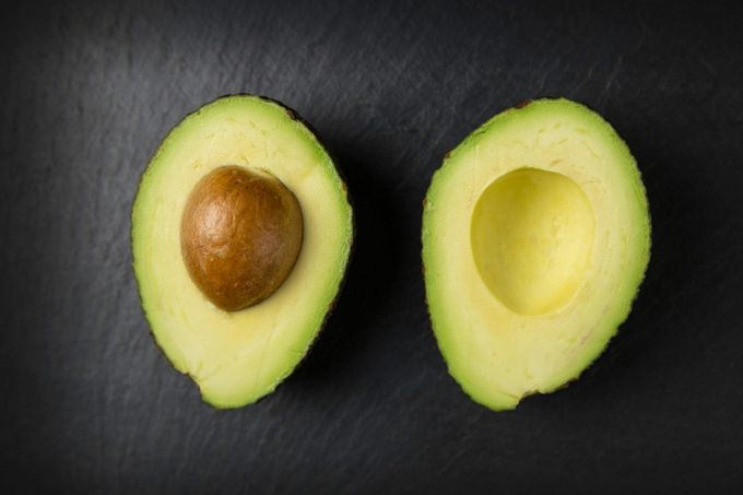 an avocado cut in half on a black surface