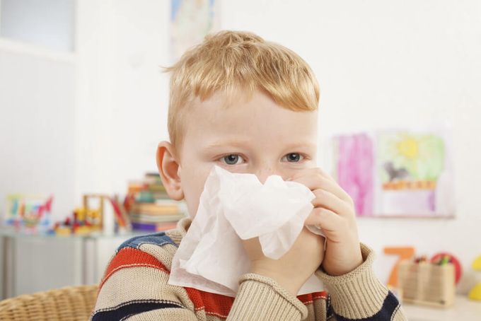 A young boy blowing his nose indicating that he's sick.
