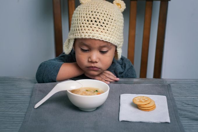 A little boy sitting at a table with a bowl of soup and crackers.