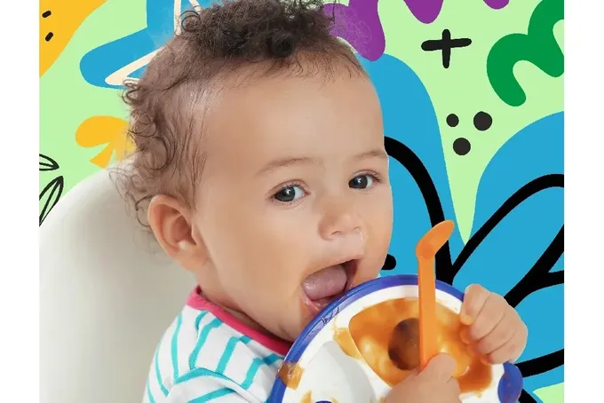 A baby in a high chair holding a spoon in it's mouth.