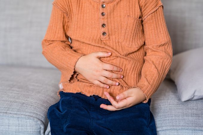 A little boy sitting on a couch with his hands on his stomach.