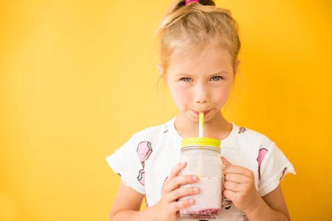 A little girl drinking a healthy shake with a yellow background.