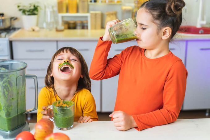 a couple of kids sitting at a table with a green smoothie