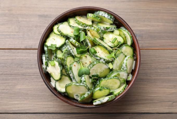A bowl of cucumber salad on top of a wooden table.