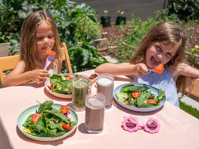 two little girls sitting at a table with plates of food