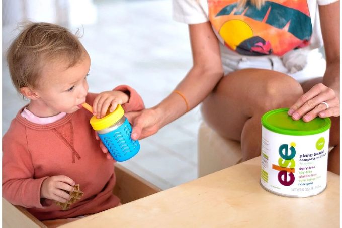 a little girl sitting at a table with a bottle