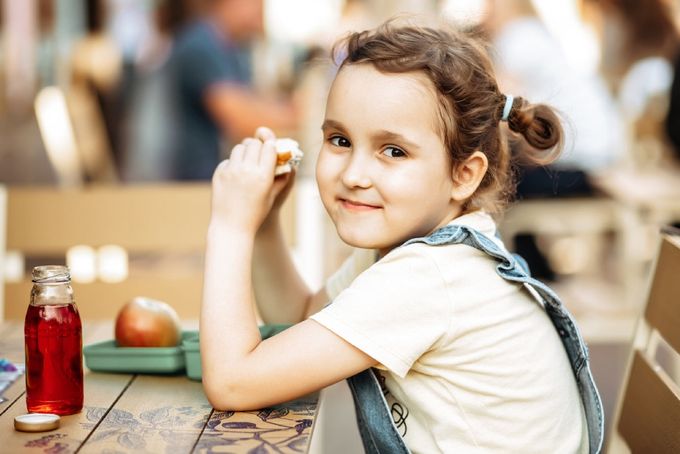 a little girl sitting at a table with a jar of fruit