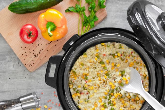 a crock pot filled with rice and vegetables next to a cutting board