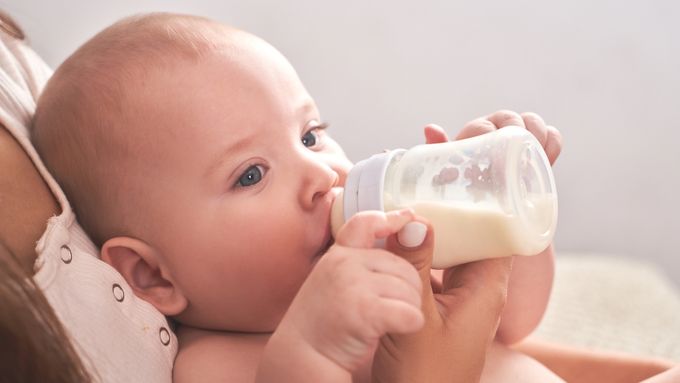 A baby drinking from a bottle while laying on a bed.