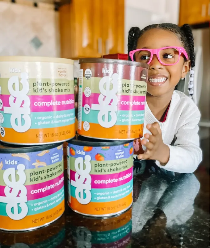 a little girl wearing pink glasses holding up a stack of baby formulas