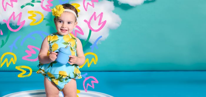 a little girl in a yellow and blue swimsuit holding a blue frisbee