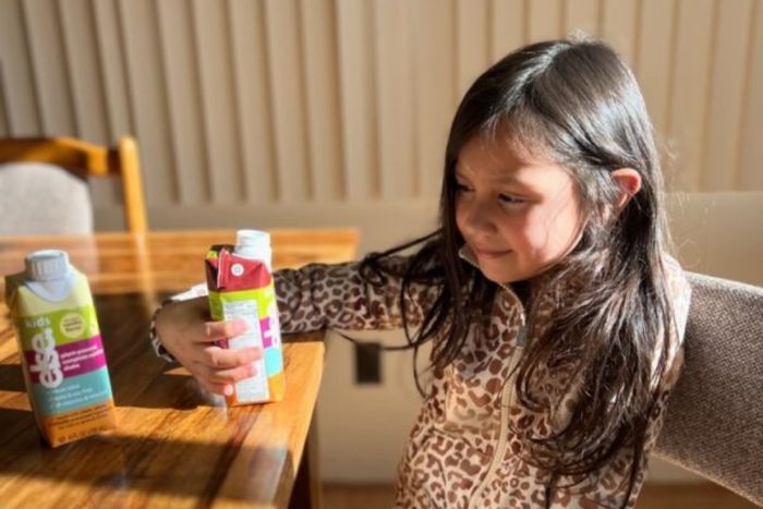 a little girl holding a bottle of Else Ready to drink shake on a table